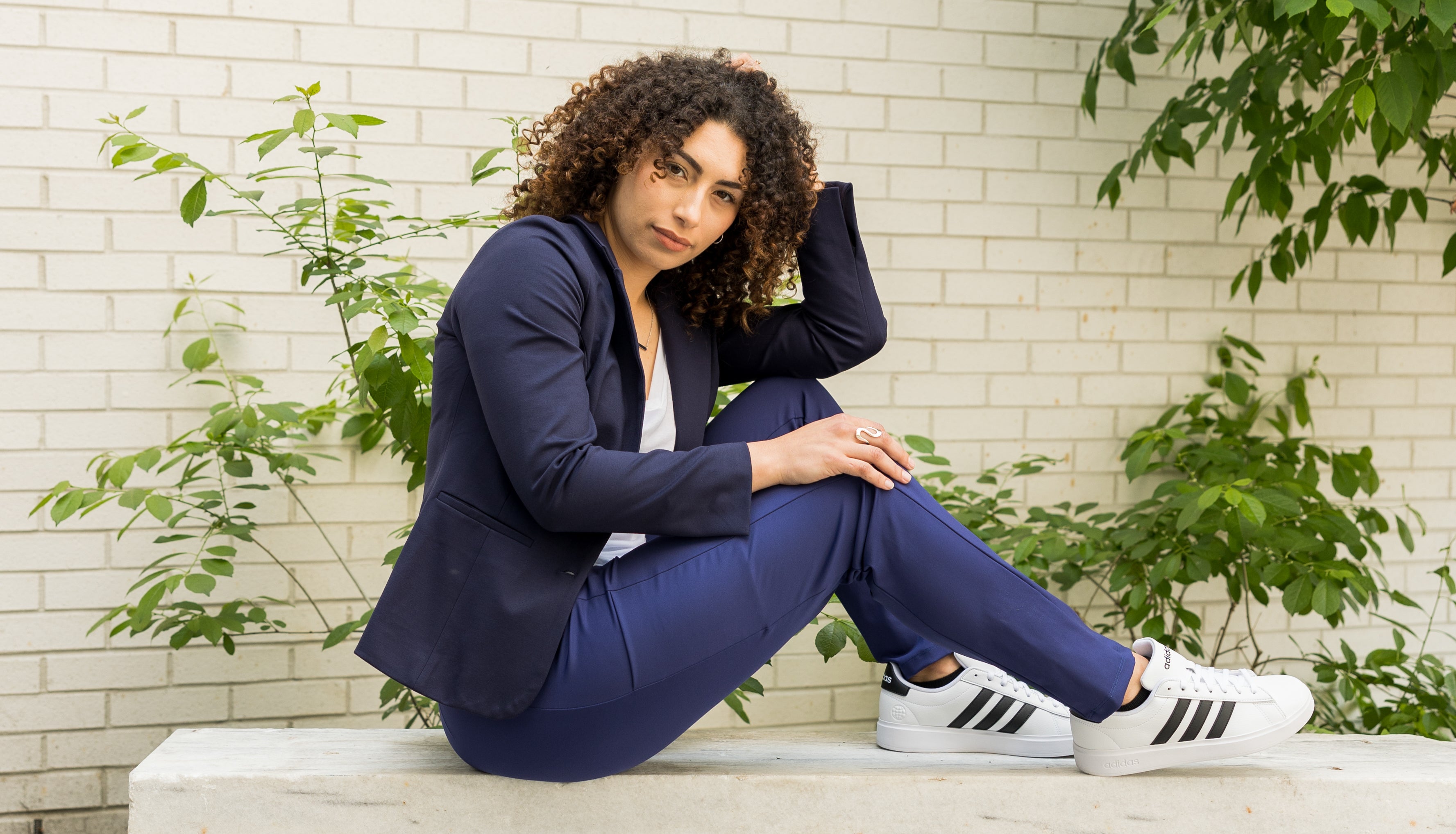 Fashionable woman in a tailored blazer and trousers, posing in a modern, minimalist setting, highlighting SISU's commitment to flexible, elegant wardrobes.